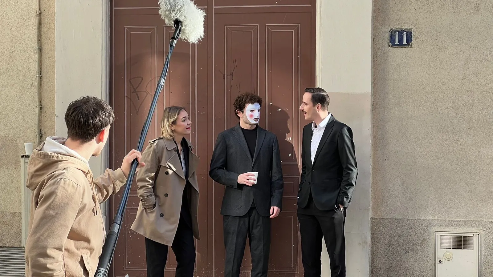 Tournage en extérieur : comédien au masque blanc entouré de l'équipe